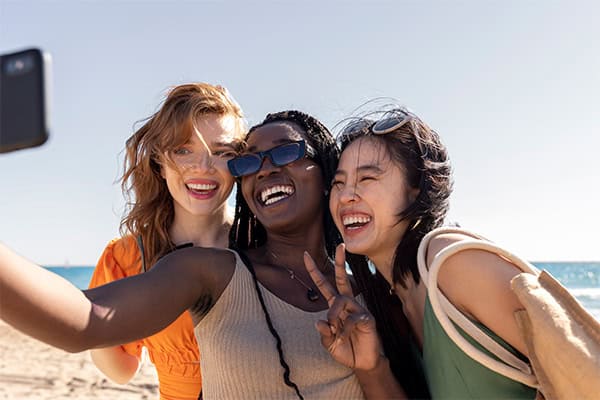 cape-town-tours-bucketlist Three women smiling and taking a selfie on the beach with Table Mountain in the background.