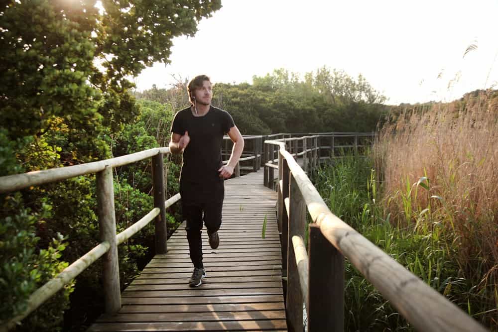 Century City Attractions 5 A man jogging on a wooden boardwalk surrounded by lush greenery and tall grass, bathed in warm sunlight.