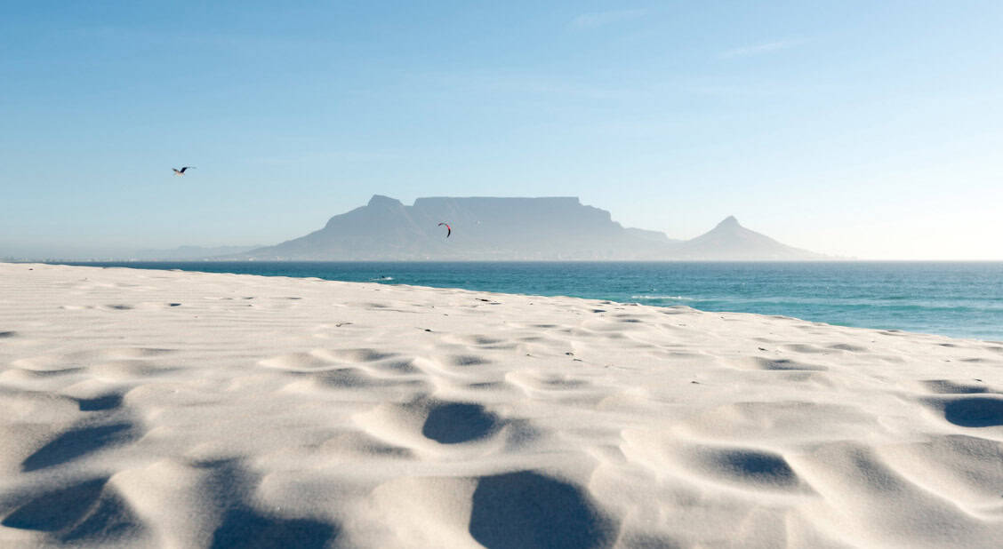 beaches-of-cape-town Breathtaking view of the top beaches in Cape Town featuring pristine white sand beaches, the sparkling ocean, and the iconic Table Mountain and Lion's Head in the background.