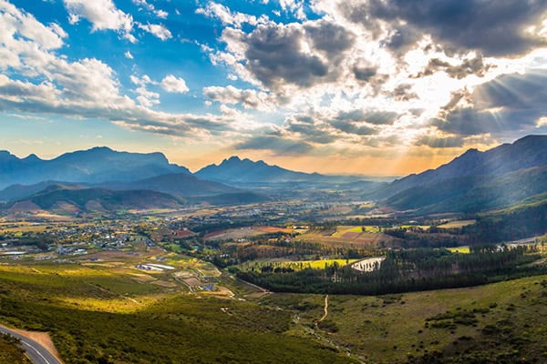 cape-town-winelands A scenic view of a valley surrounded by mountains, with clouds gently drifting across the sky above.
