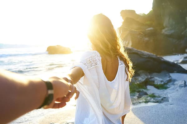 couple-on-the-beach Couple holding hands while walking into a bright sunshine on the beach