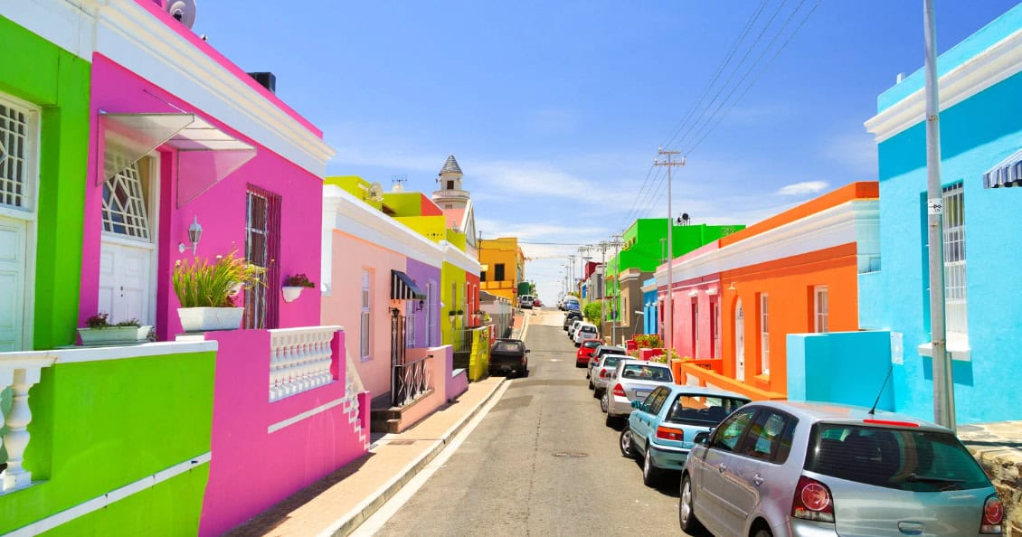 hidden-gems-cape-town A vibrant street featuring a row of colorful houses, each painted in cheerful hues, creating a lively atmosphere.