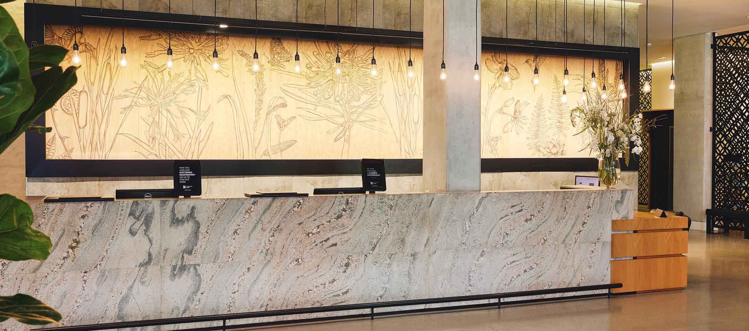 The elegant reception at Century City Hotels features a marble desk, warm lighting, floral décor and intricate wood paneling.