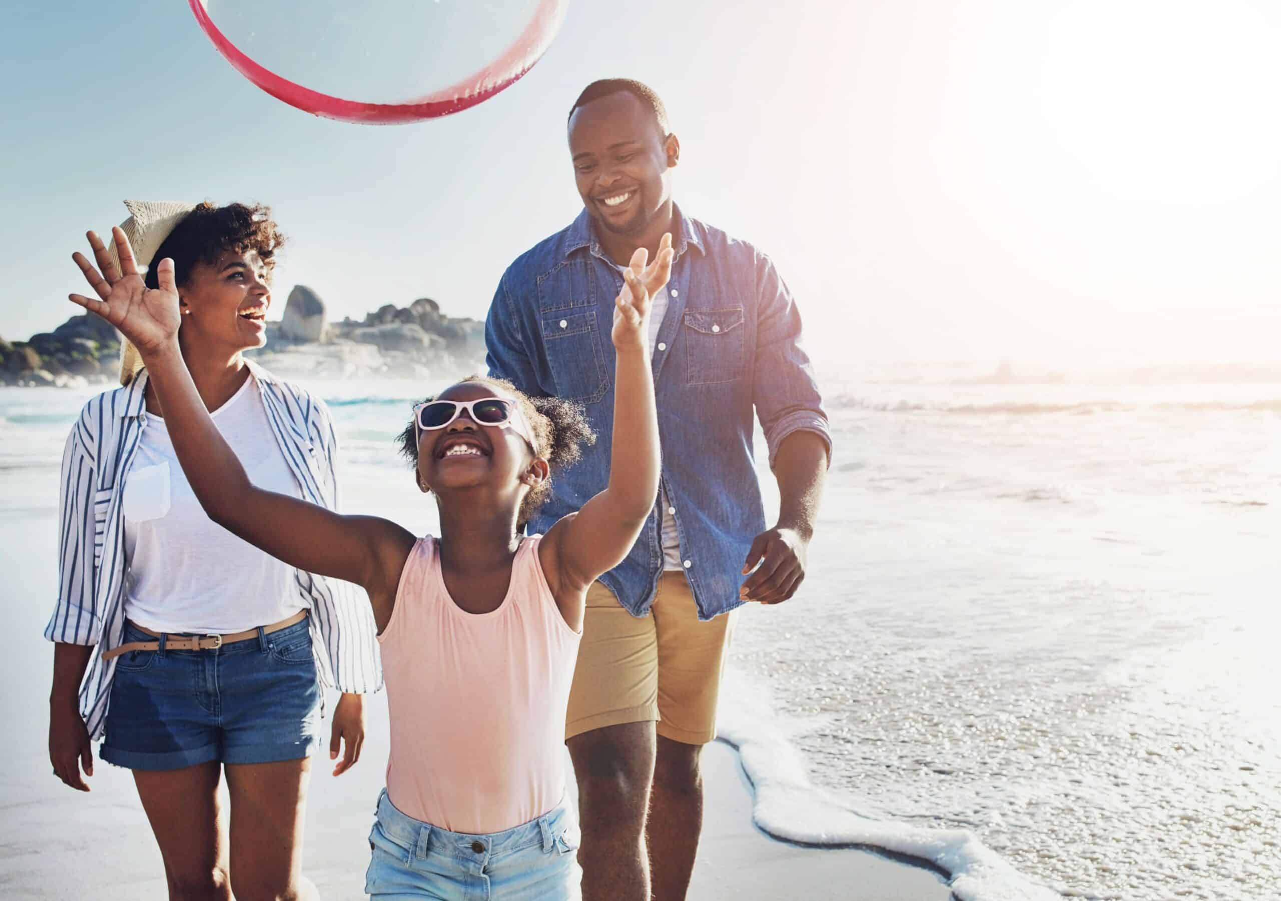 happy-hoop-family-by-beach-vacation-adventure-holiday-bonding-summer-fun-smile-african-girl-child-with-parents-playing-with-plastic-ring-toy-by-ocean-weekend-trip (1) A family of 3 strolling on a beach near one of the family-friendly hotels in Cape Town