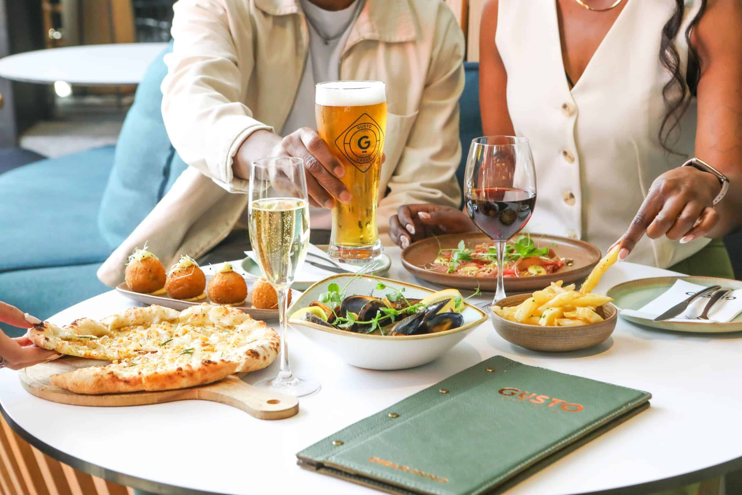 G (1) A table arrayed with a variety of sharing plates in front of a stylish couple for dinner in Cape Town Restaurants