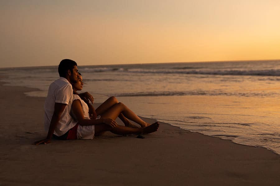 couple-looking-sea-beach-sunset A couple enjoying the sunset while sitting on the beach during romantic getaways in Cape Town