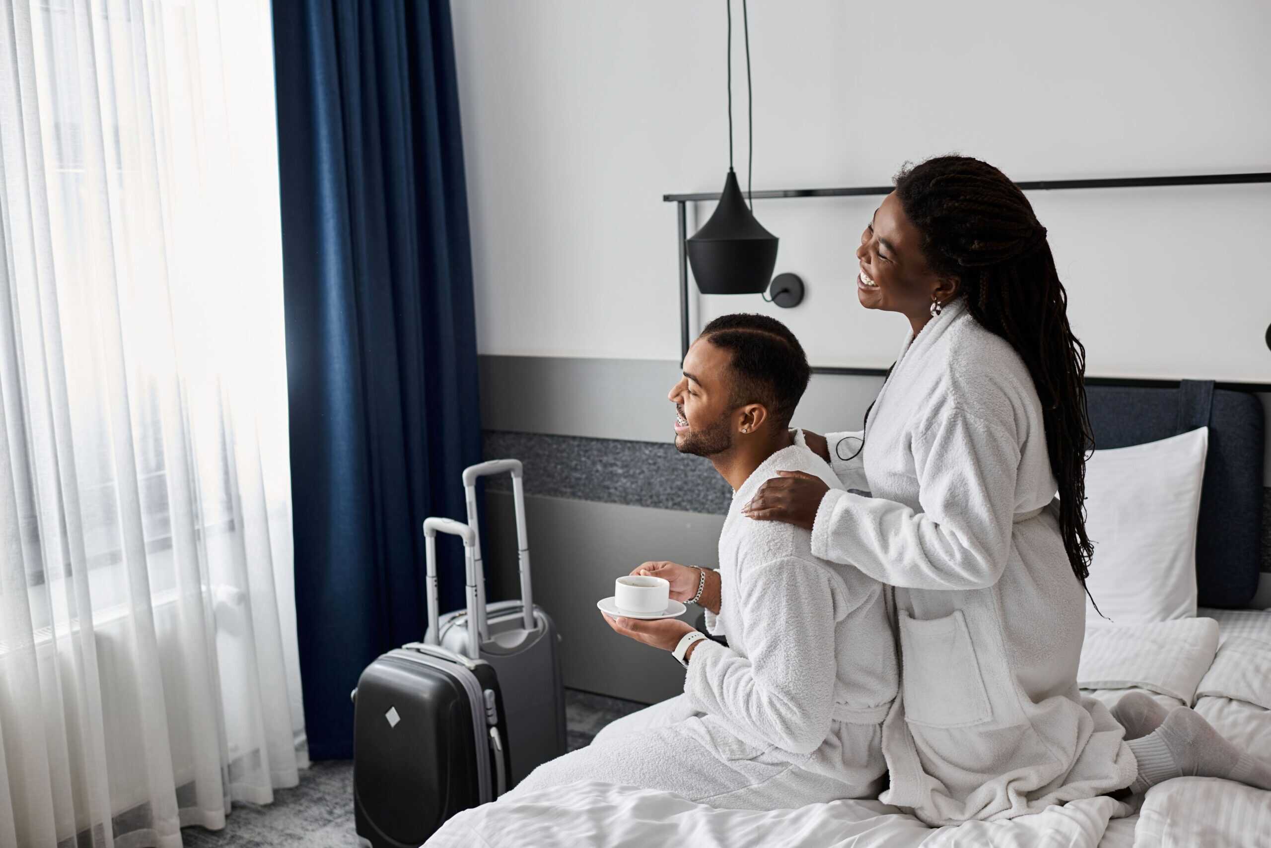 joyful-couple-enjoying-cozy-moments-chic-hotel-room-vacation (1) A mixed couple wearing white bathroom gowns and enjoying affordable accommodation Cape Town