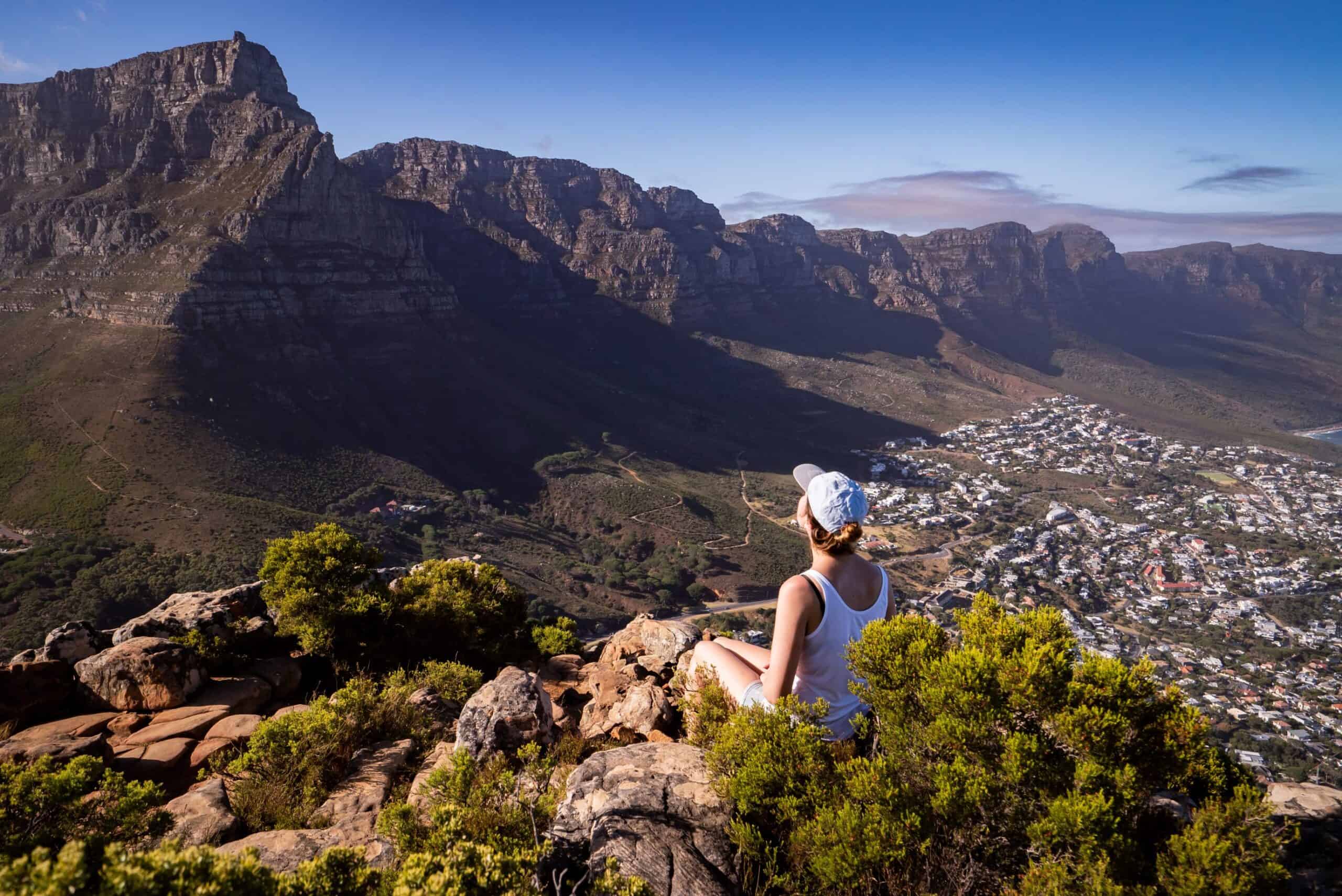 beautiful-shot-woman-sitting-edge-cliff-admiring-city-cape-town (1) A woman sitting on the edge of a cliff, admiring outstretched Cape Town views.